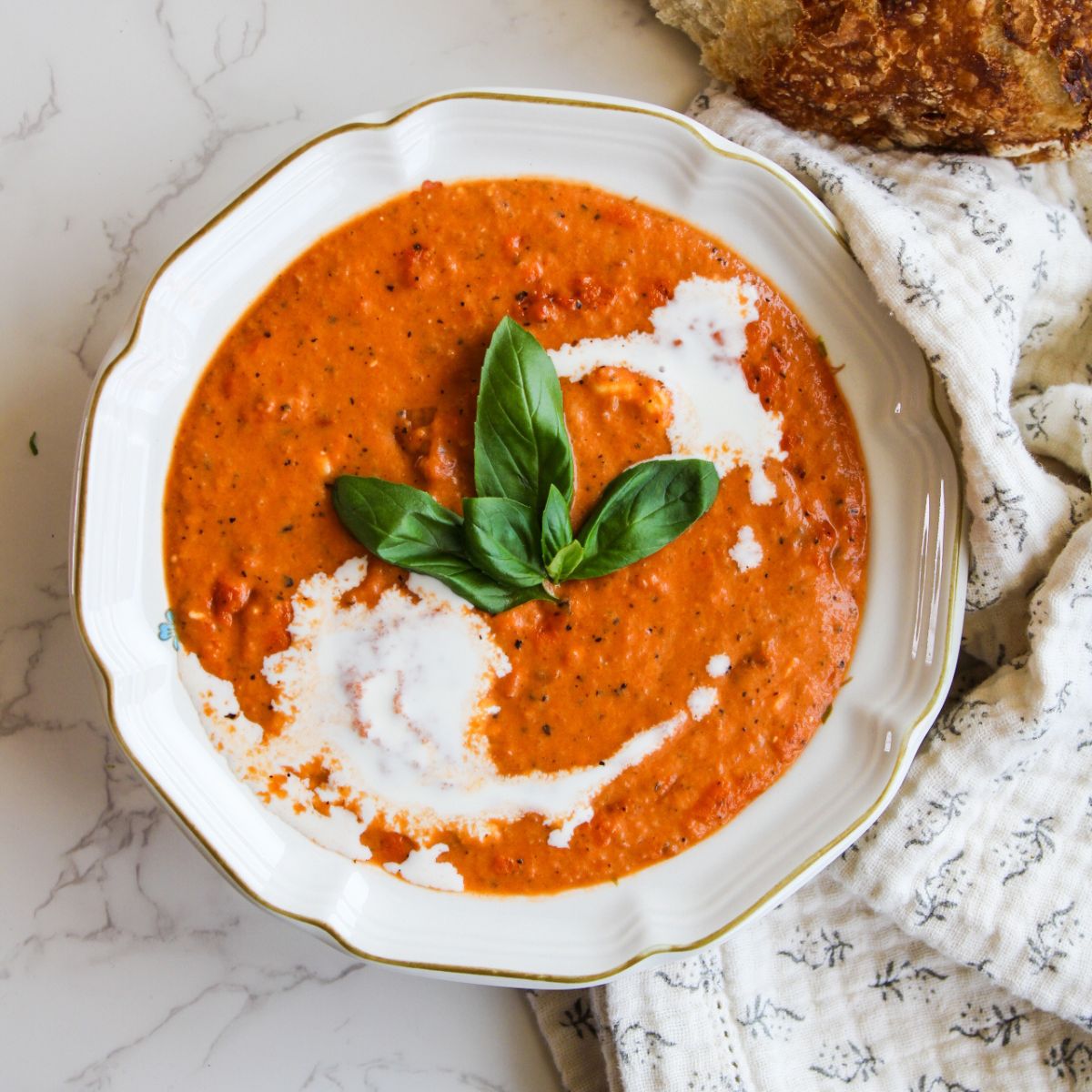 A bowl of tomato soup with cream drizzled on top and 3 basil leafs on top, too.