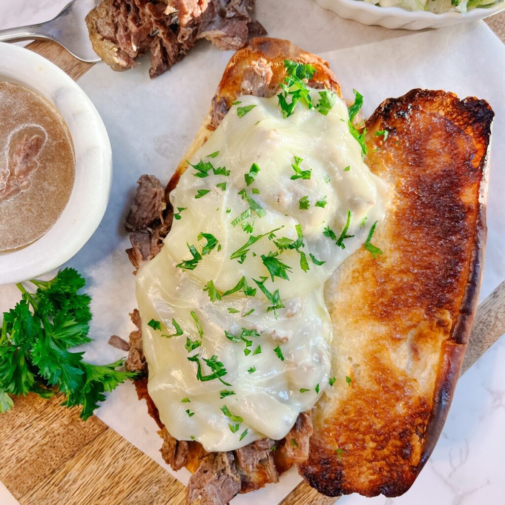 Top the french dip sandwich with melted provolone and fresh parsley.