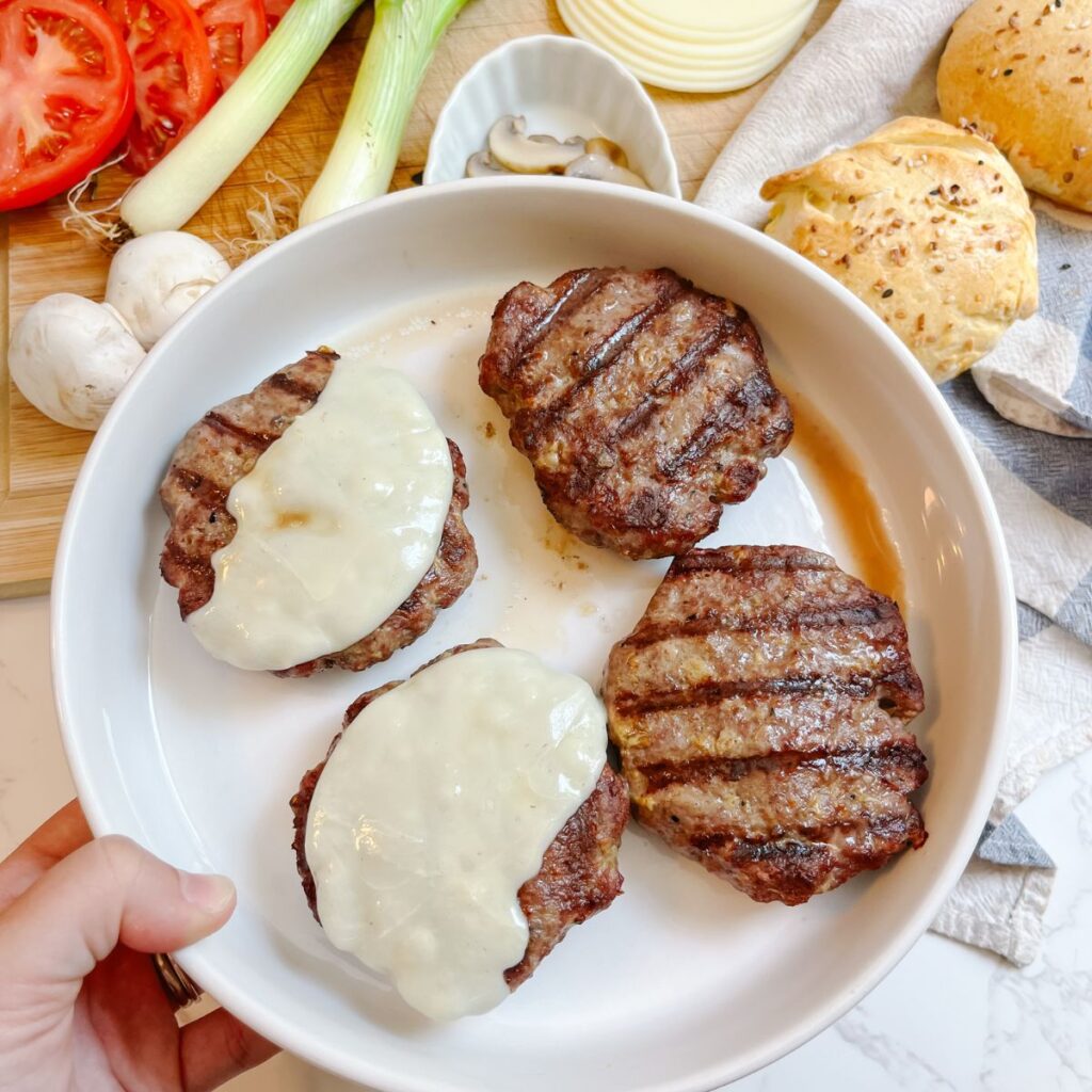 A plate of homemade hamburgers. Top them with cheese.