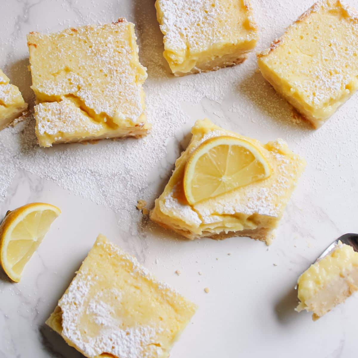 Yellow lemon bars with a dusting of powdered sugar and fresh lemon slices as garnish.