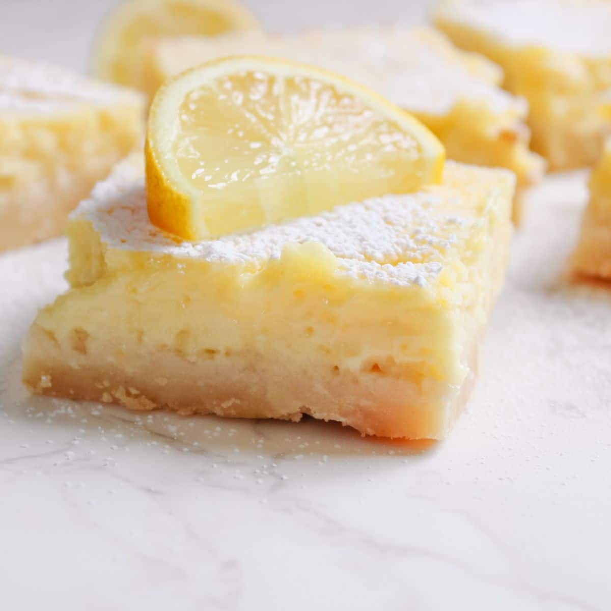 Lemon cream cheese bars have a shortbread base, are topped with powdered sugar and garnished with fresh lemon slices.