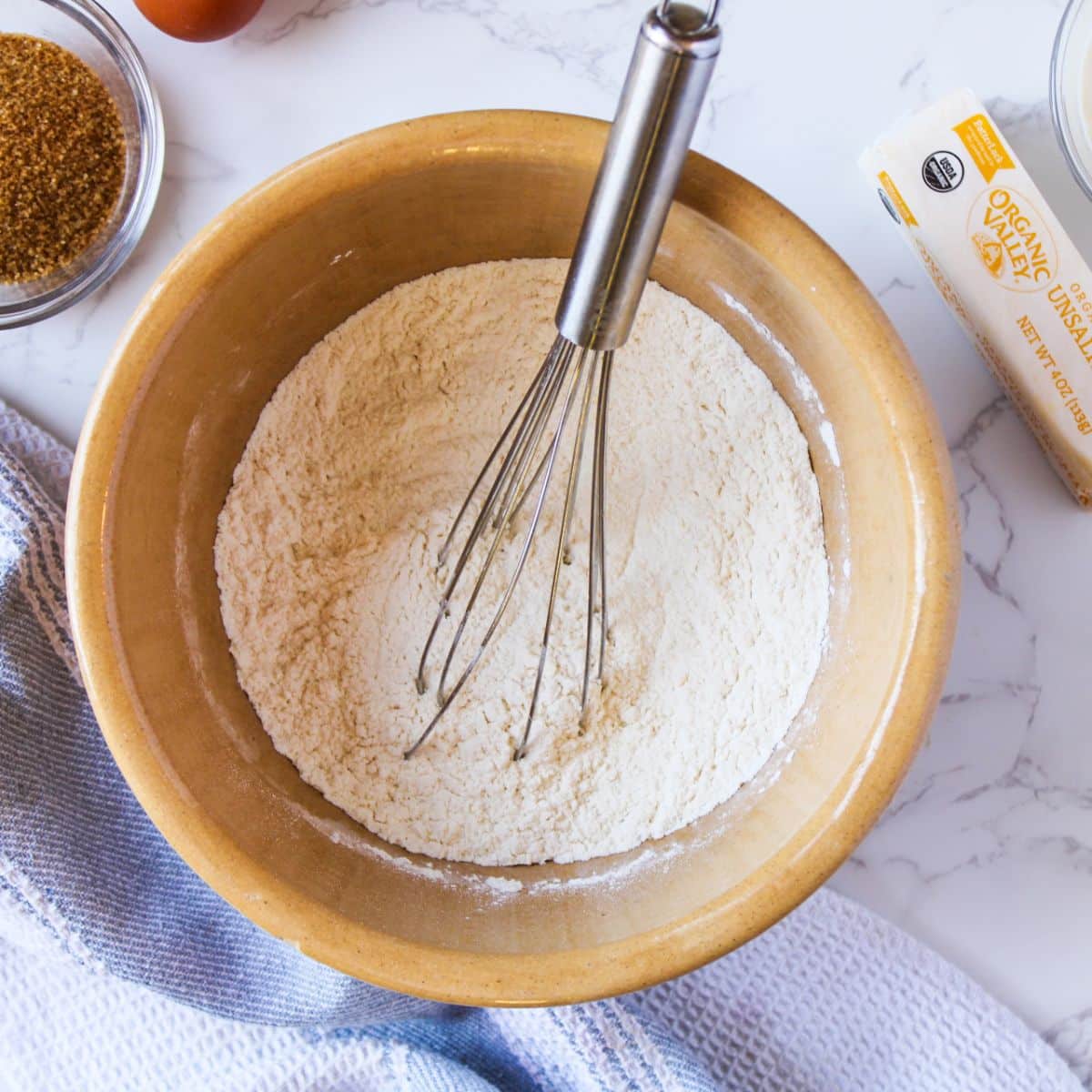 Whisk together the dry ingredients in a large mixing bowl. This is a large bowl with flour and baking powder being whisked with a silver whisk.