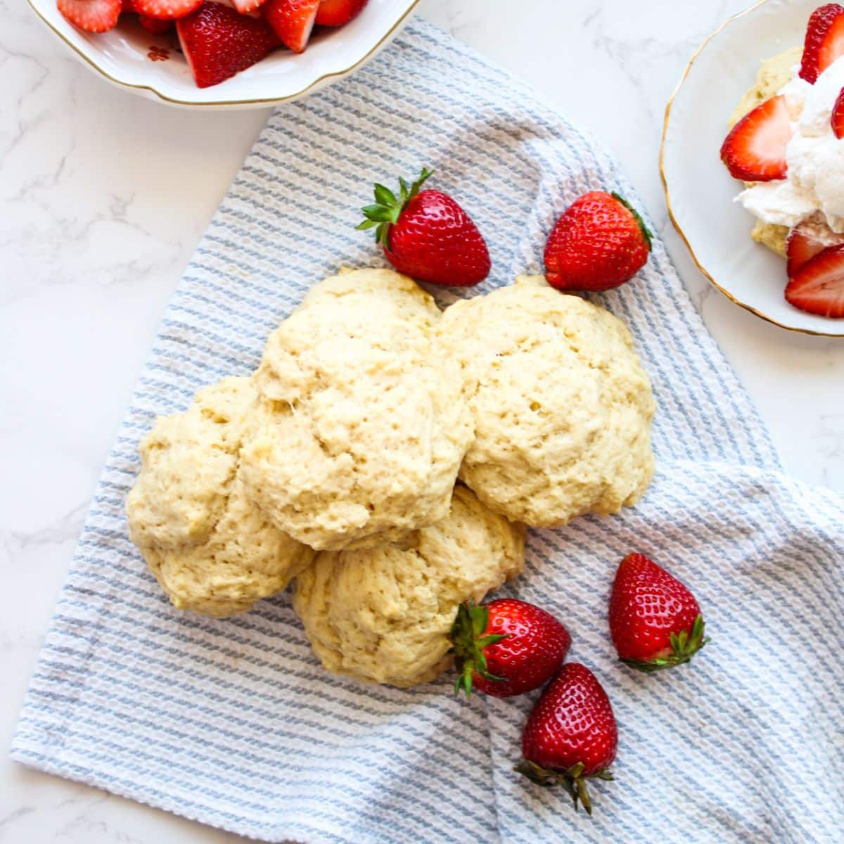 Baked sourdough shortcakes on a tea towel with whole strawberries scattered around.