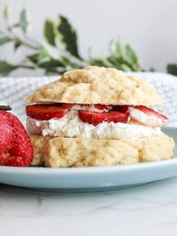 A sourdough strawberry shortcake sliced in half with homemade whipped cream and strawberry slices in the middle of the two halves, kind of like a sandwich.