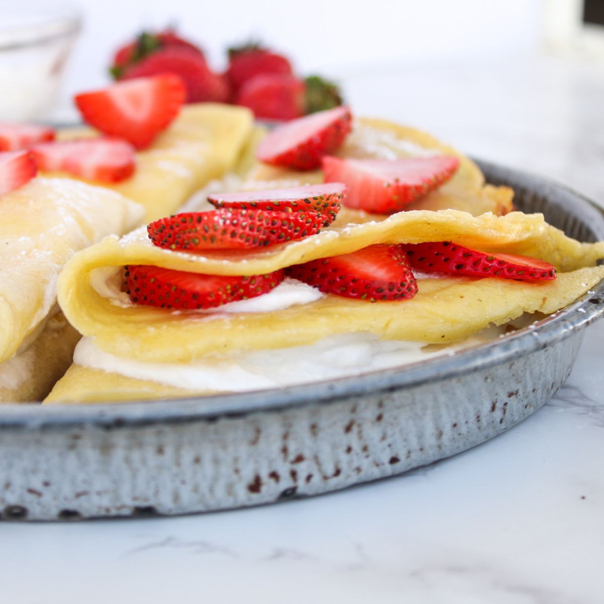 A sourdough discard crepe folded into a triangle, sitting on a gray plate, and stuffed with whipped cream and fresh strawberry slices.