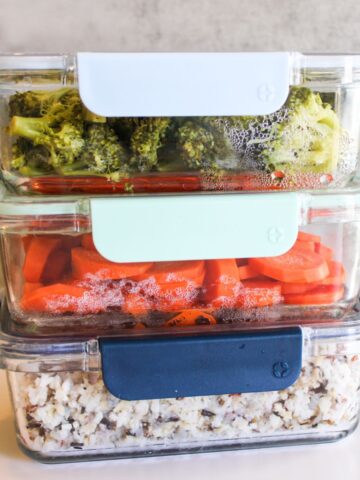 3 non toxic food containers that are glass and stacked on top of each other. The top one has broccoli, the middle one is filled with carrots and the bottom one is full of rice.