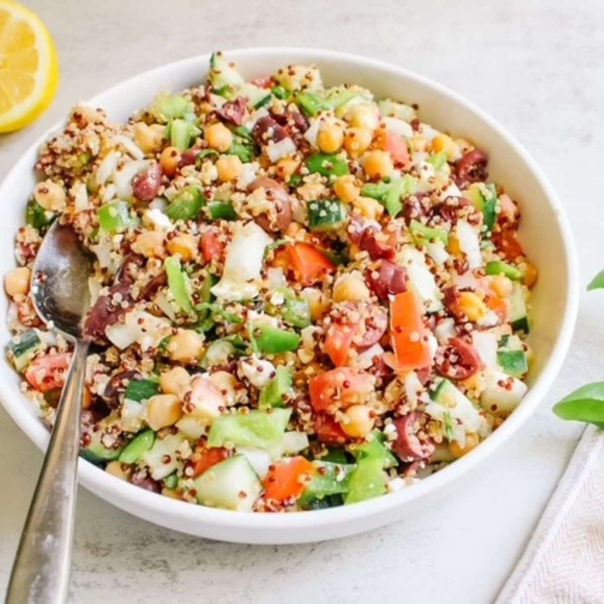 A white bowl filled with quinoa cucumber tomato salad with a silver spoon.