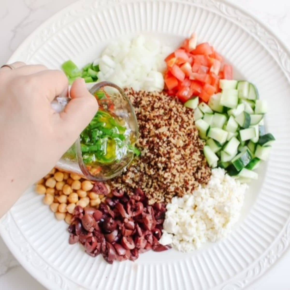 Pour homemade salad dressing over the quinoa, olives, feta, cucumber, tomato, white onion, green pepper, and chickpeas.