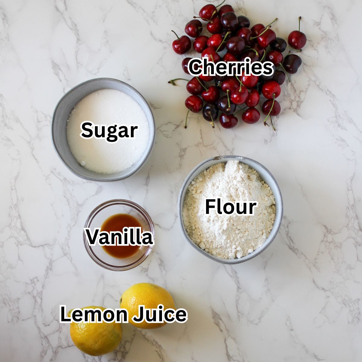 A bowl of sugar, fresh whole cherries, a bowl of flour, a small bowl of vanilla extract and 2 lemons.