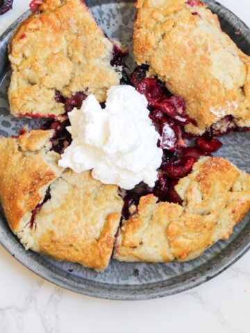 A gray plate holding 5 slices of a cherry galette with a dollop of whipped cream in the middle.