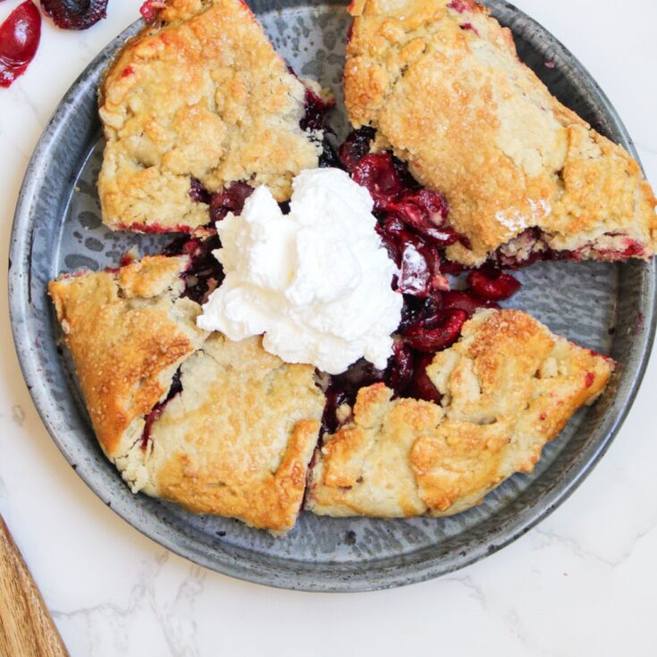A gray plate holding 5 slices of a cherry galette with a dollop of whipped cream in the middle.