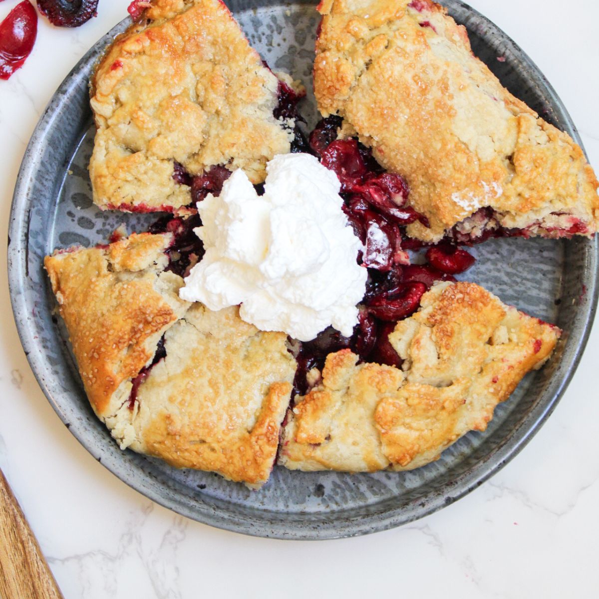 A gray plate holding 5 slices of a cherry galette with a dollop of whipped cream in the middle.