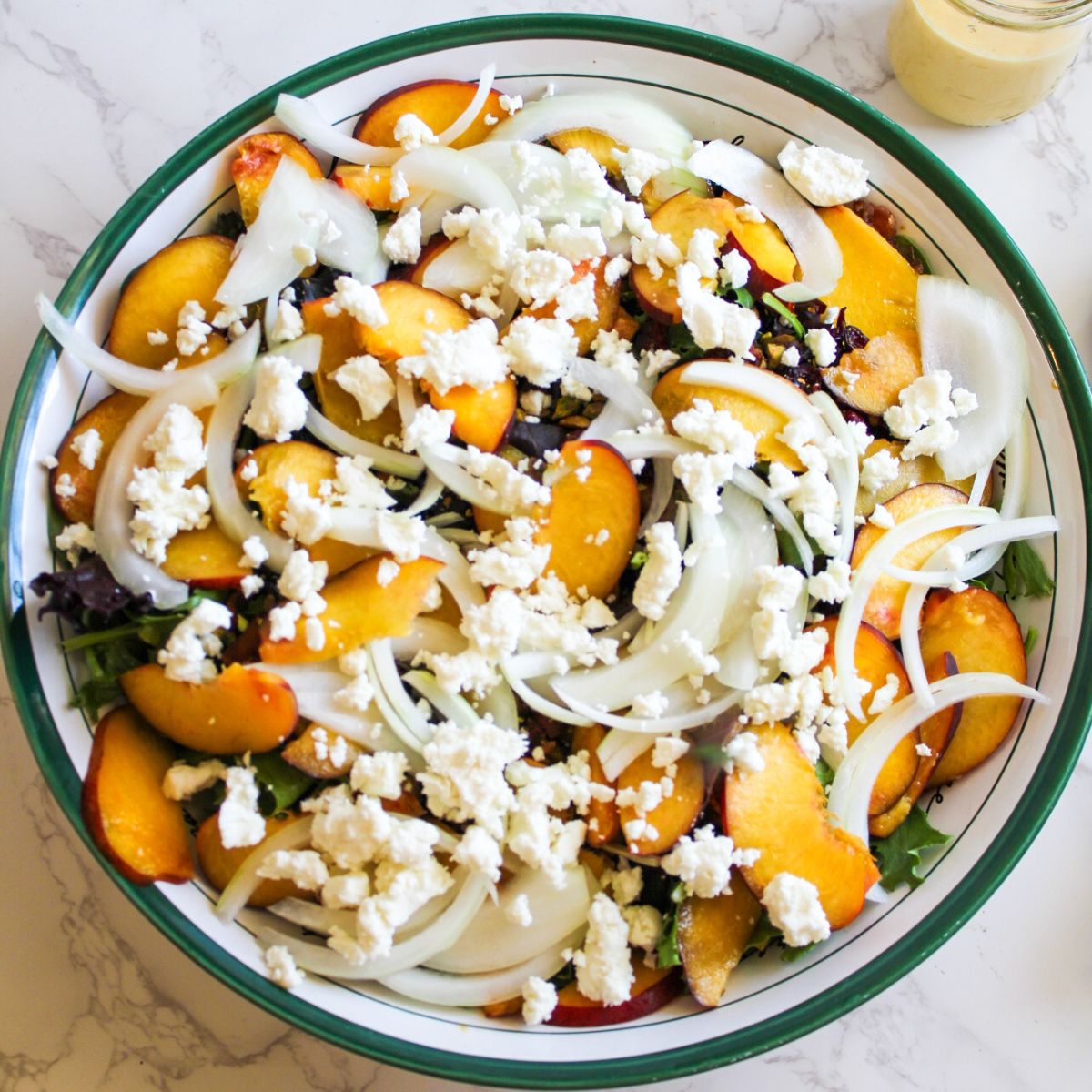 Crumble goat cheese all over the top of the peaches, greens, sliced onions, nuts, and cranberries. 