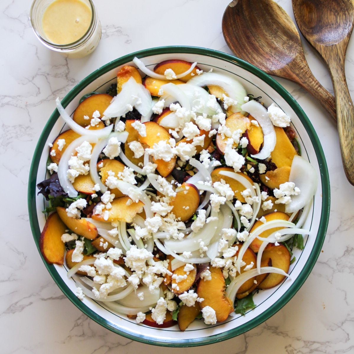 A large salad bowl with a peach goat cheese salad and wooden salad servers along with a peach vinaigrette.