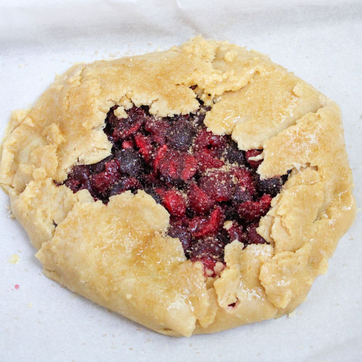 A cherry galette sprinkled with brown sugar on a baking sheet lined with parchment paper.