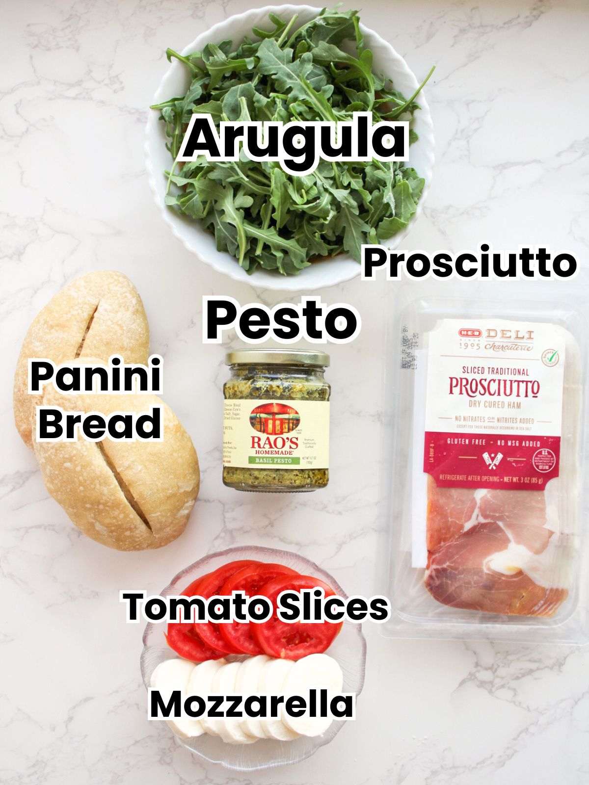 Ingredients for a pesto panini-arugula, prosciutto, pesto, panini bread, tomato slices, mozzarella cheese