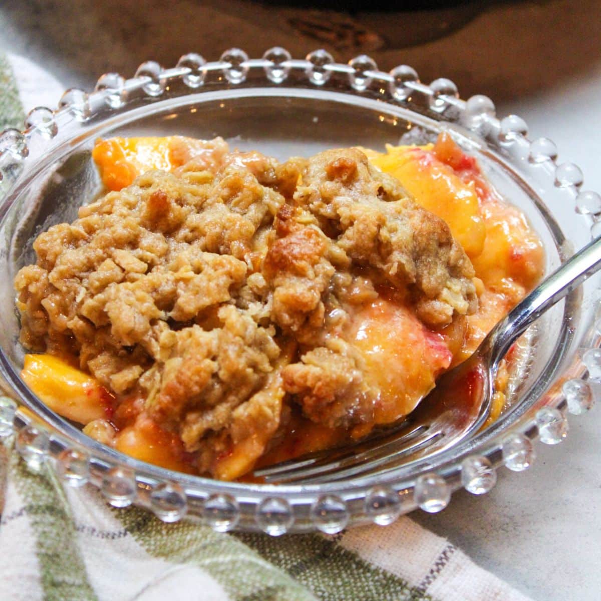 A glass bowl with peach crisp and a silver fork.