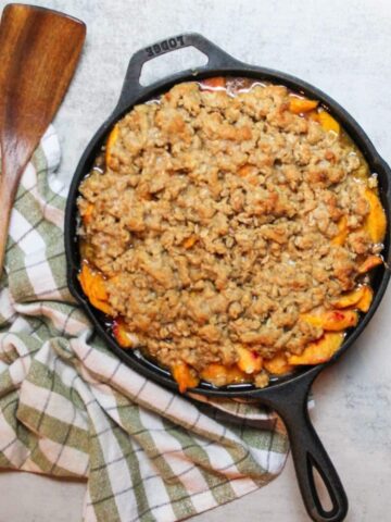 Peach crisp in a cast iron skillet with a wooden serving spoon.