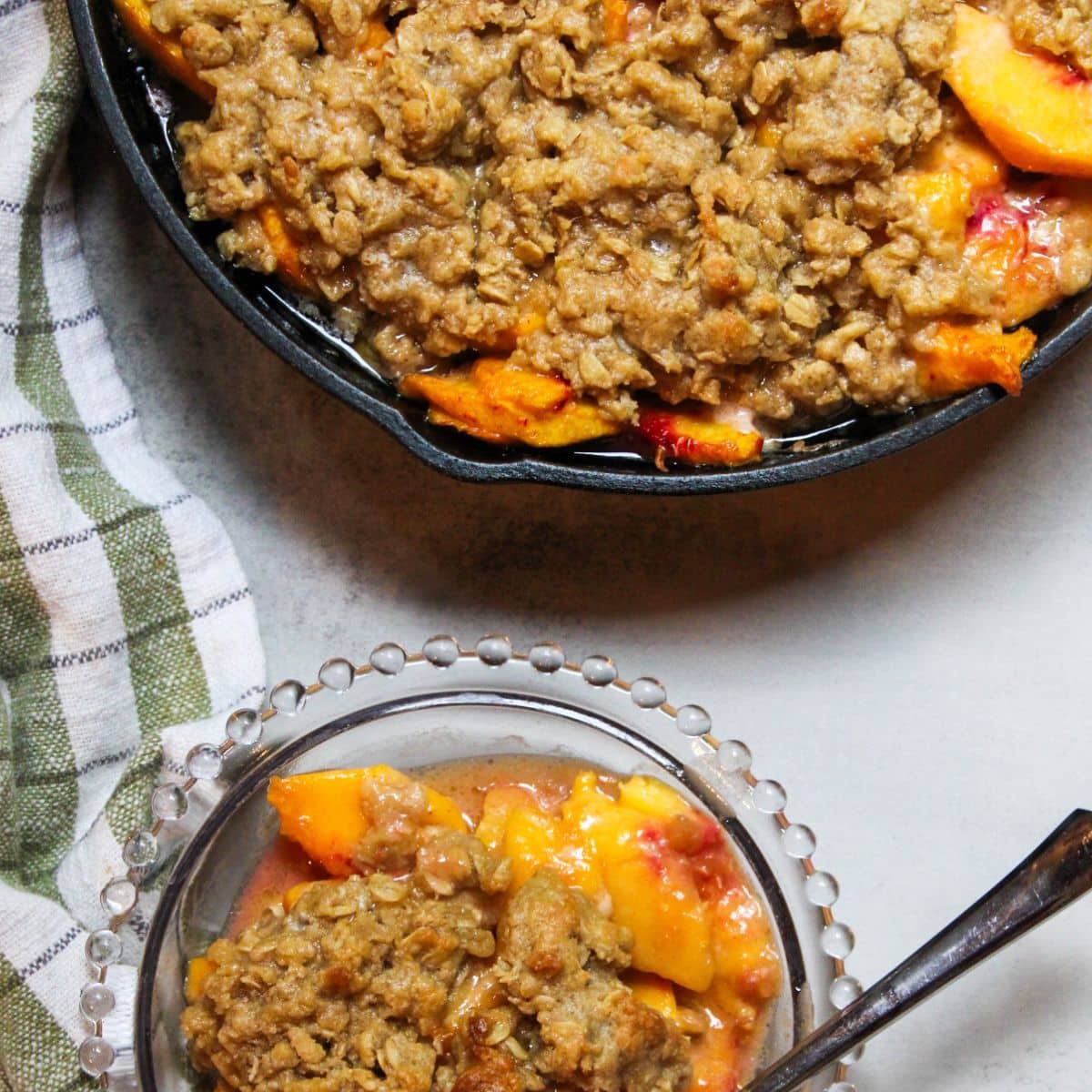 Peach crisp in a cast iron skillet and a small plate with some peach crisp.