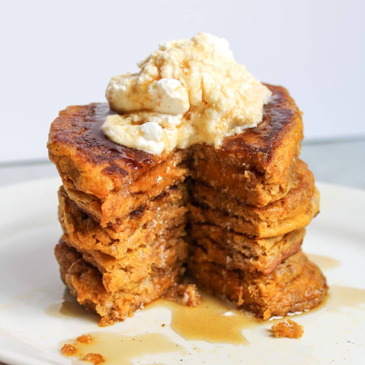 A stack of sourdough pumpkin pancakes topped with whipped cream and maple syrup, sitting on a white plate.