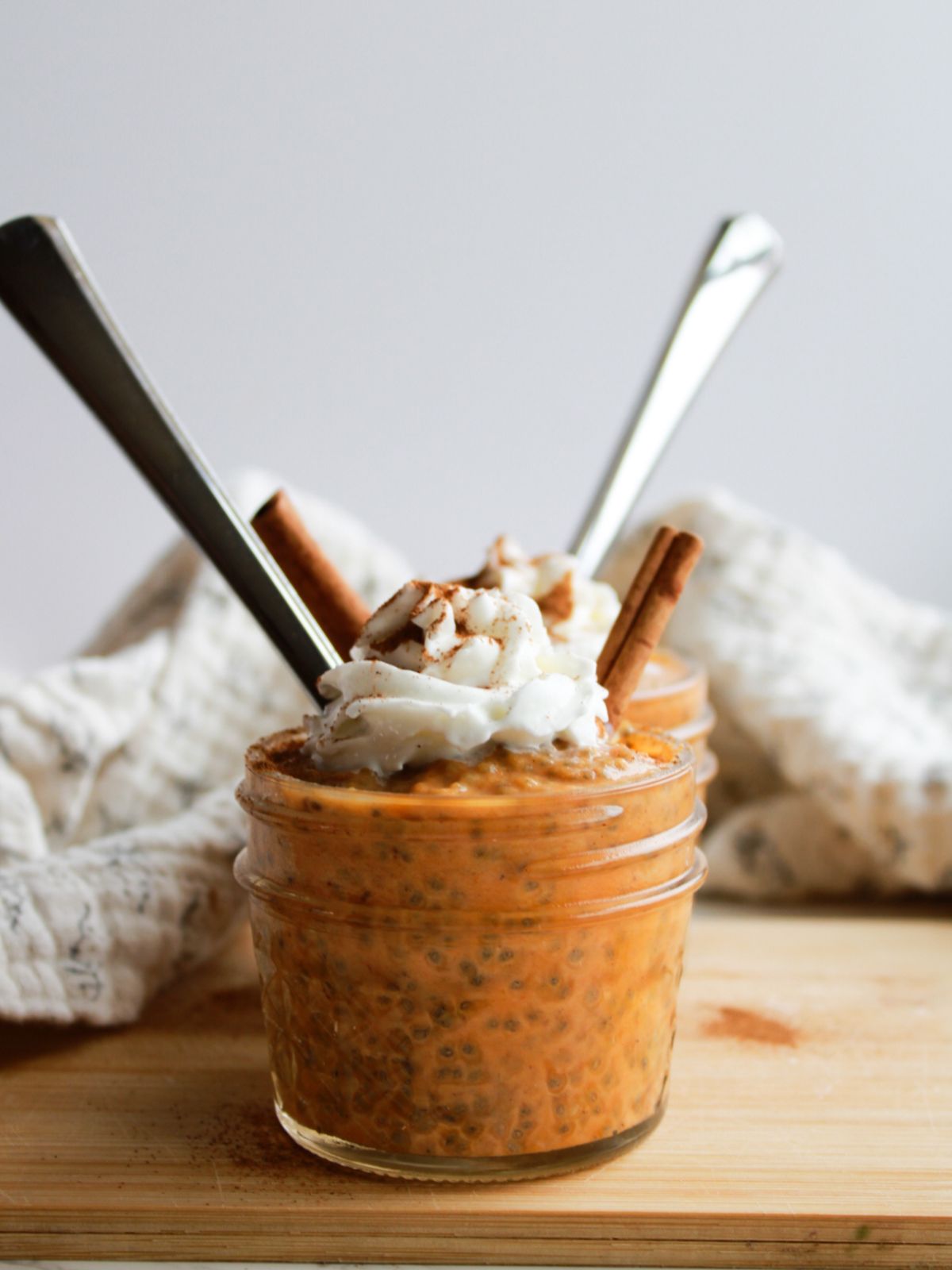 A mason jar filled with chia seed pudding and topped with whipped cream and a cinnamon stick. There's a silver spoon sitting in the bowl too.