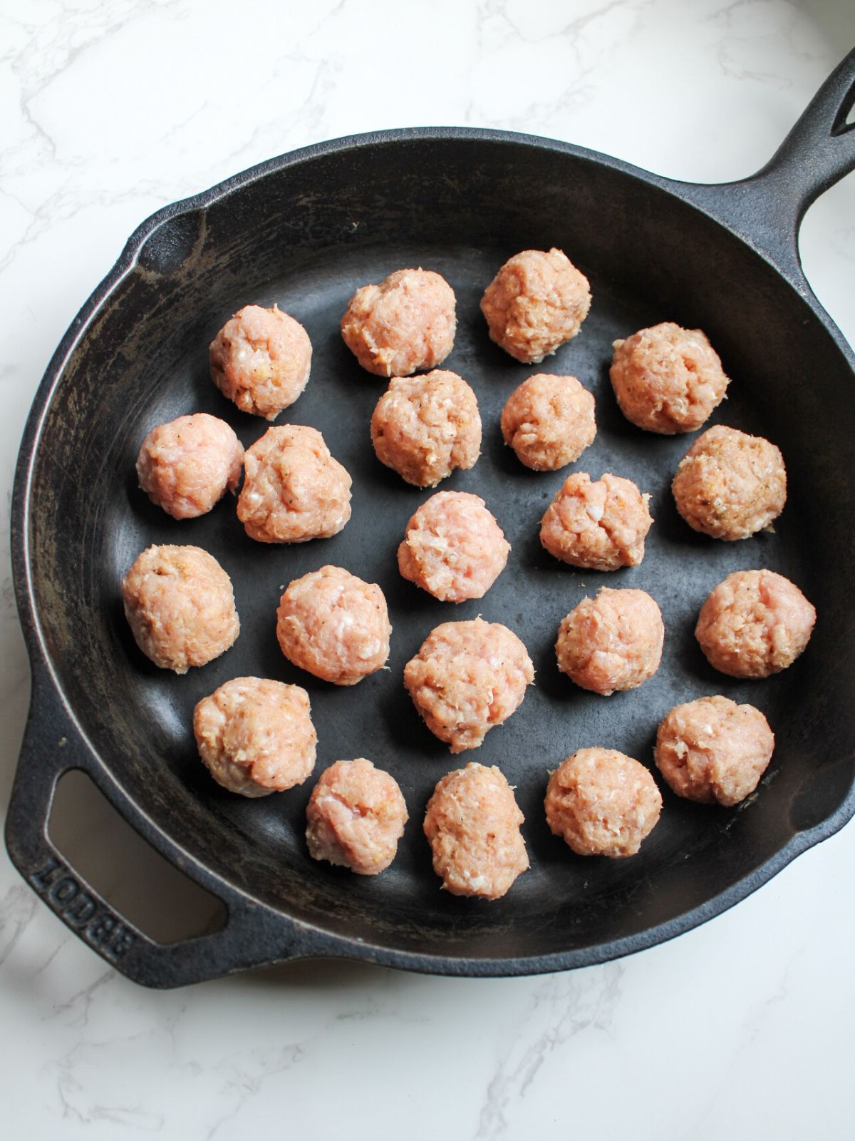 A black cast iron skillet filled with mini meatballs that aren't cooked yet.