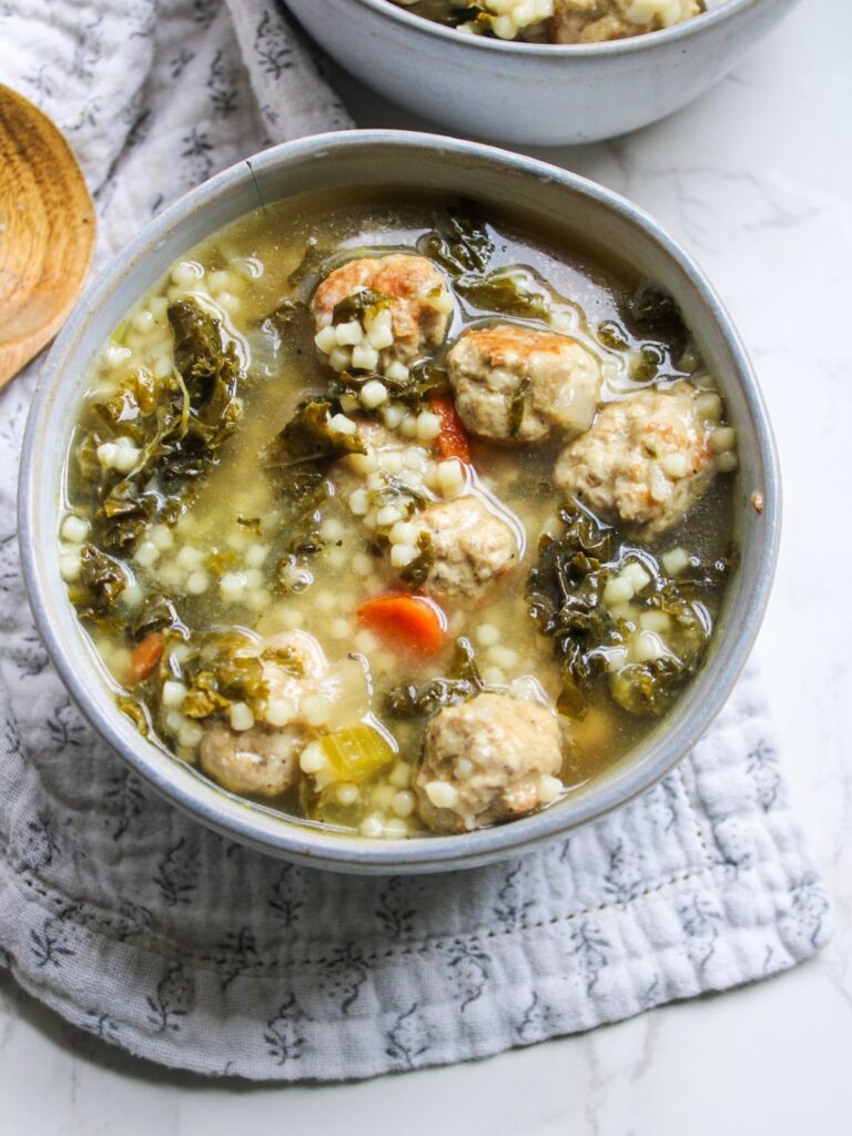 A gray bowl, sitting on a gray floral napkin, filled with Italian wedding soup.