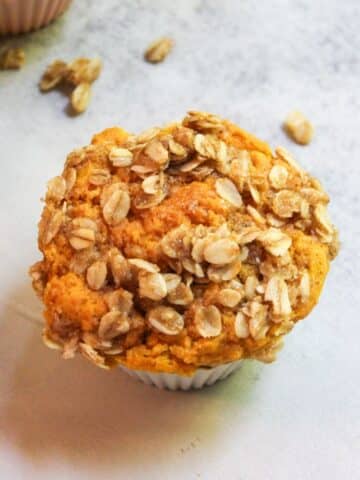 A sourdough pumpkin muffin that has a brown sugar streusel topping, in a white muffin liner