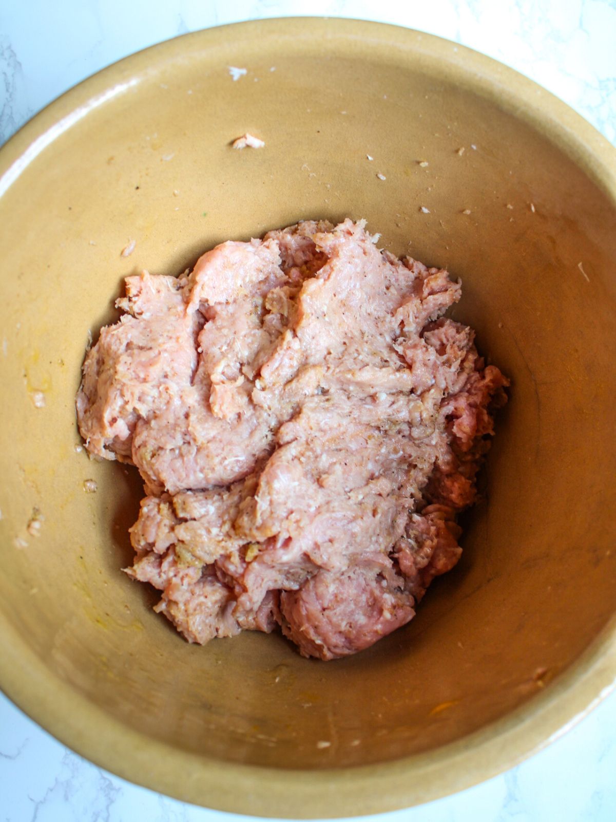 A large mixing bowl filled with ground pork, ground turkey, egg and breadcrumbs well mixed together.