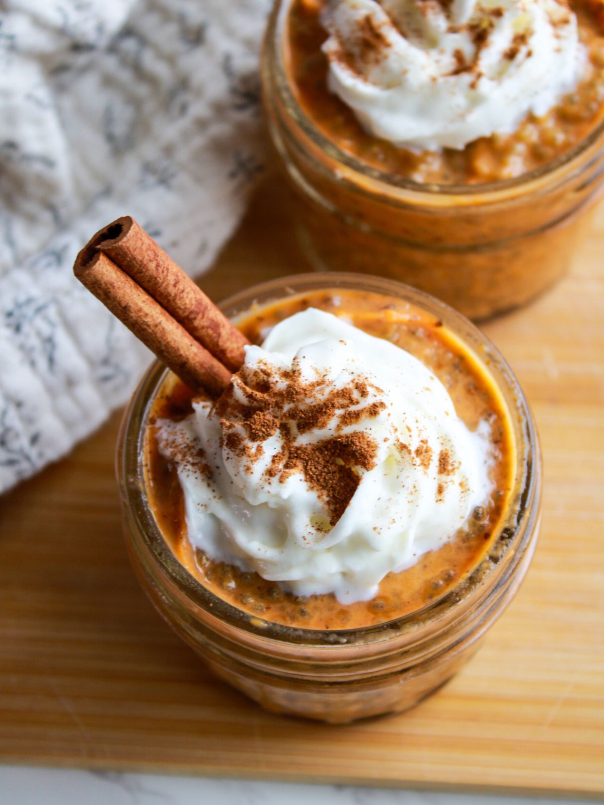A small mason jar filled with orange pumpkin chia pudding topped with whipped cream, cinnamon, and a cinnamon stick.