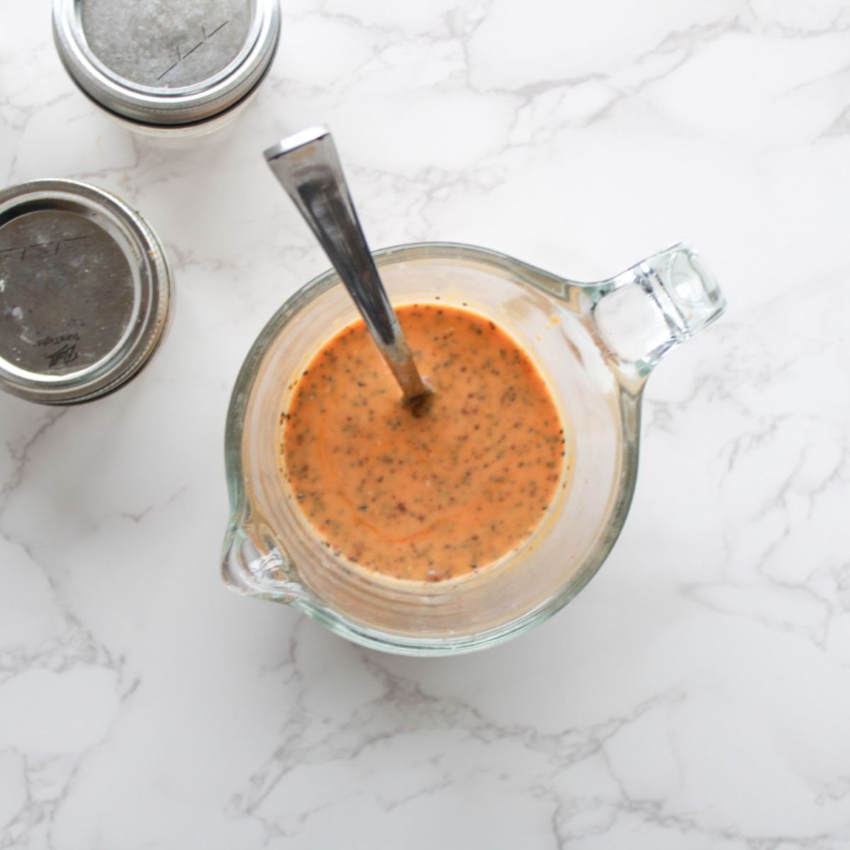 A pyrex pitcher filled with pumpkin chia pudding mix with a silver spoon.