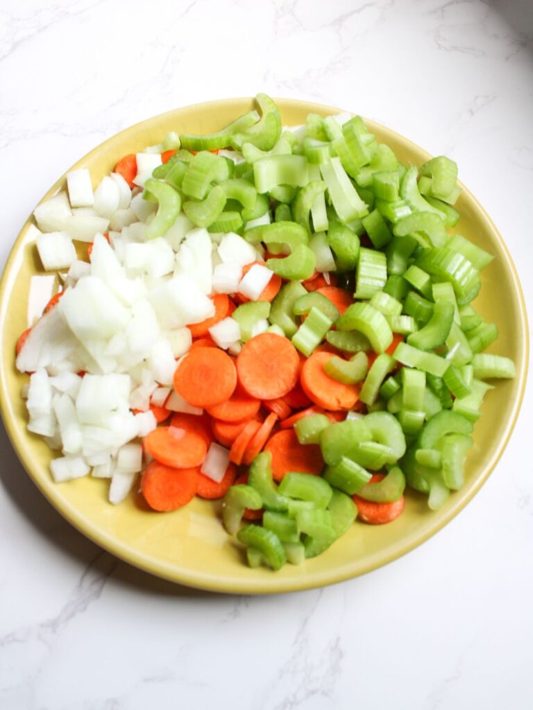 Diced onion, sliced carrots, and sliced celery on a yellow plate.