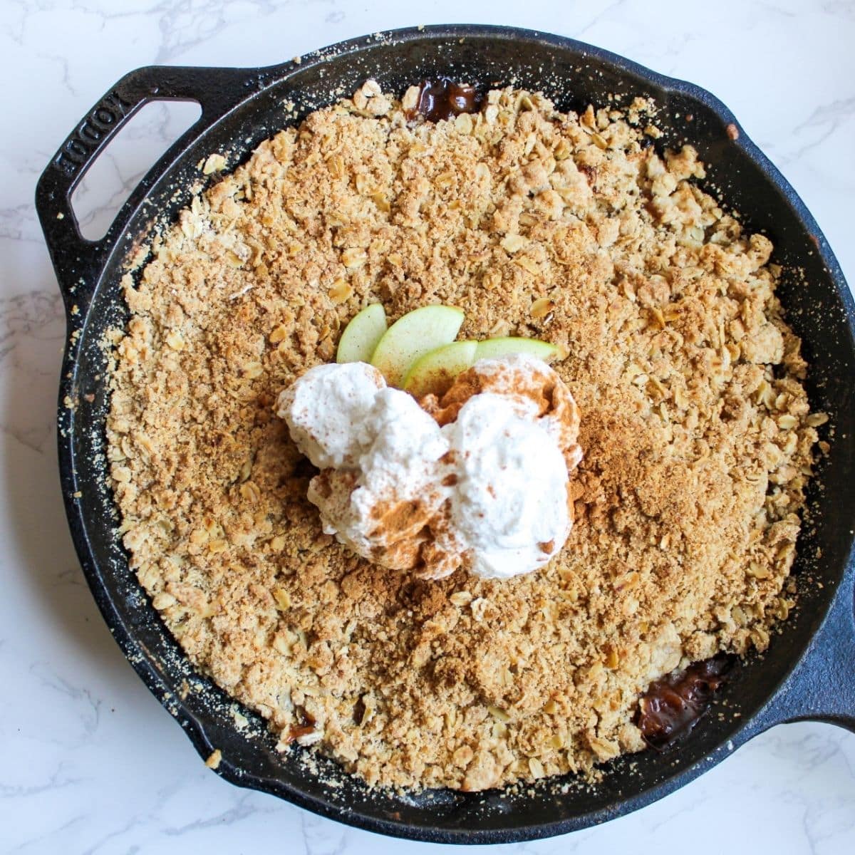 Apple crisp with oatmeal topping in a cast iron skillet, topped with whipped cream and green apple slices.