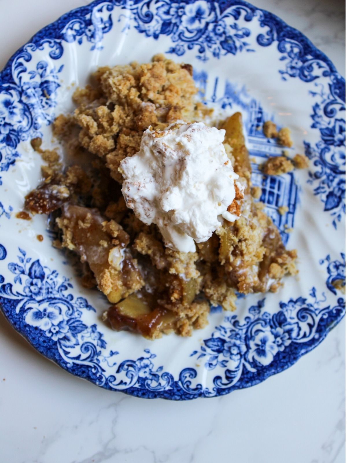Apple crisp with whipped cream on a blue and white plate.