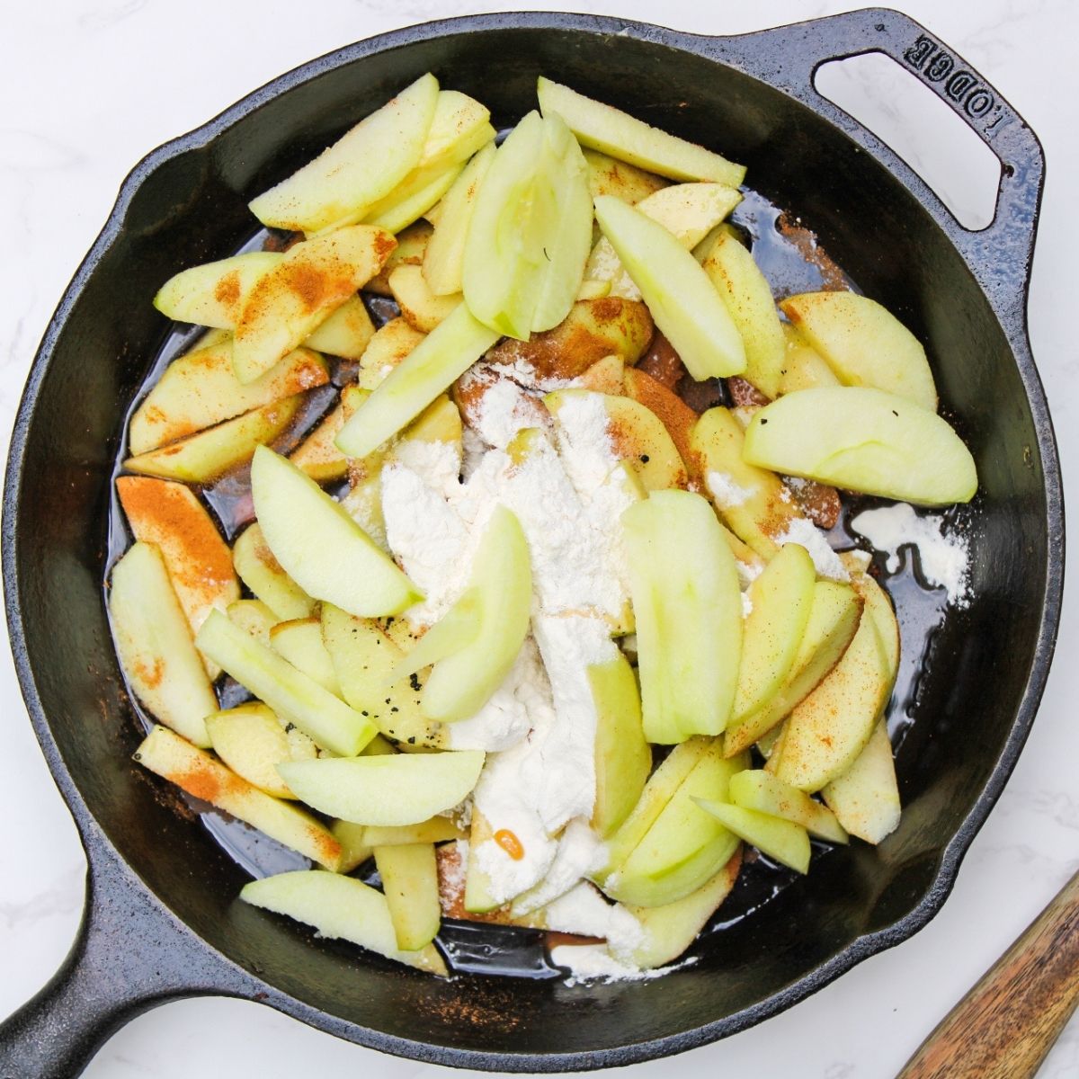 A skillet filled with apple slices, flour, maple syrup and cinnamon.